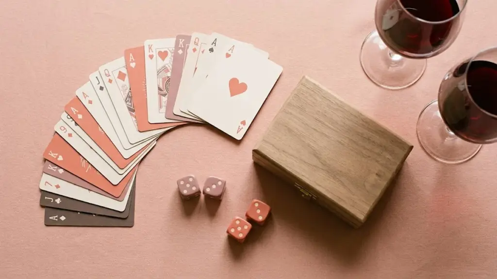 Cartas, dados y caja de juego sobre mesa con dos copas de vino, ambiente de noche de pareja