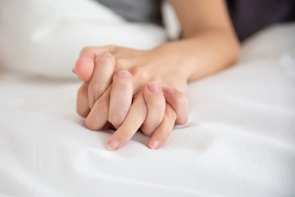 Pareja tumbada con las manos entrelazadas sobre las sábanas
